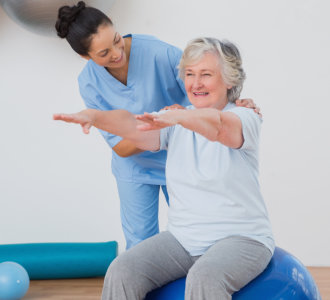 Happy instructor assisting senior woman in exercising at gym