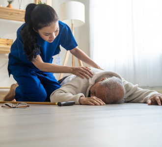 Asian caregiver helping senior male from falling on the ground at home. Elderly older patient having an accident after doing physical therapy then rescued by attractive therapist nurse in living room.