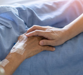 Caregiver holding elderly senior patient (ageing old adult person) hand lying in hospital bed or nursing hospice, geriatrician palliative home, while caretaker having medical health care service