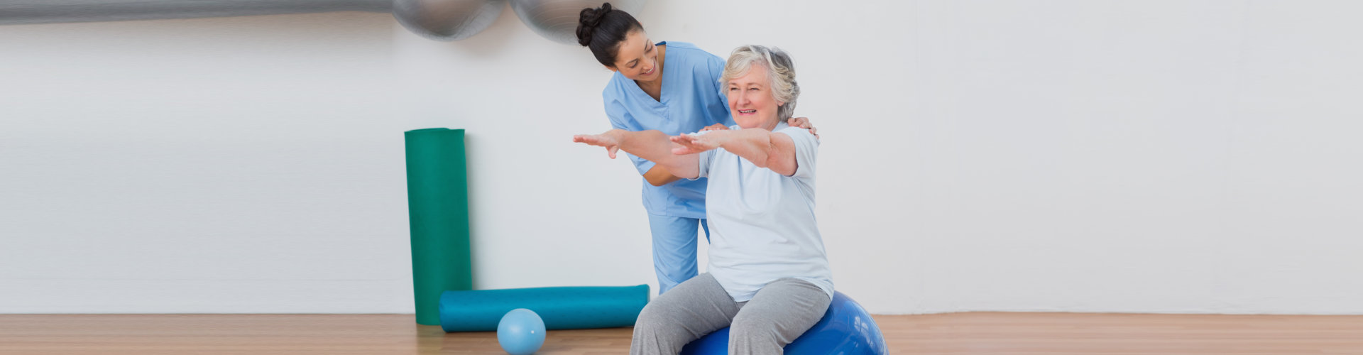 Happy instructor assisting senior woman in exercising at gym